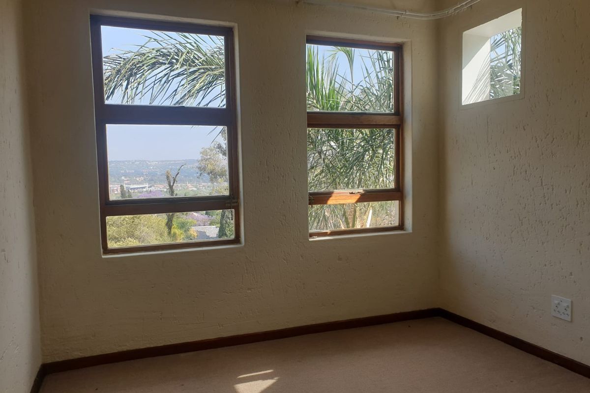 A bright, empty bedroom featuring textured walls, timber-framed windows with scenic views, and neutral carpeting.