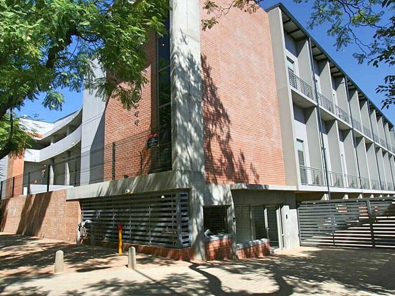 Exterior view of a modern apartment building featuring a brick and concrete facade, balconies, and secure gated entrance.