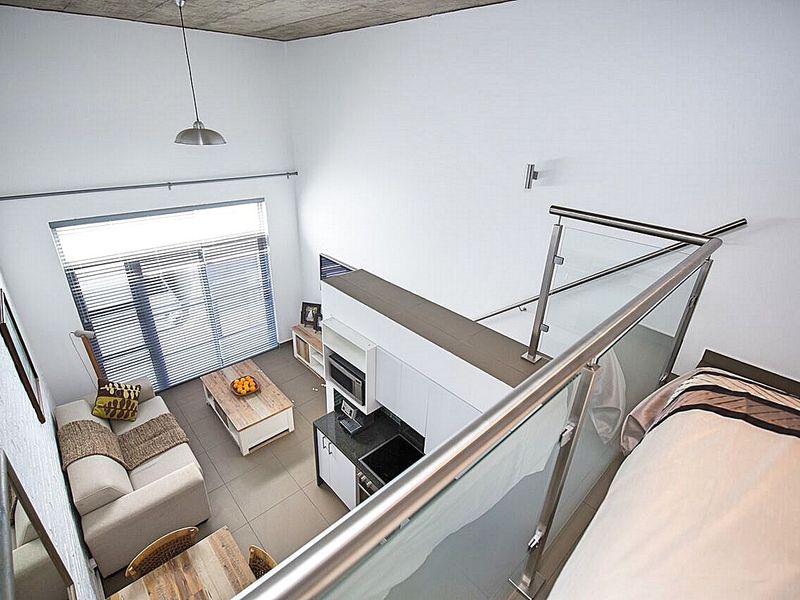 Modern open-plan apartment featuring high exposed concrete ceilings, a sleek glass balustrade overlooking the living area, and a compact, well-appointed kitchen.