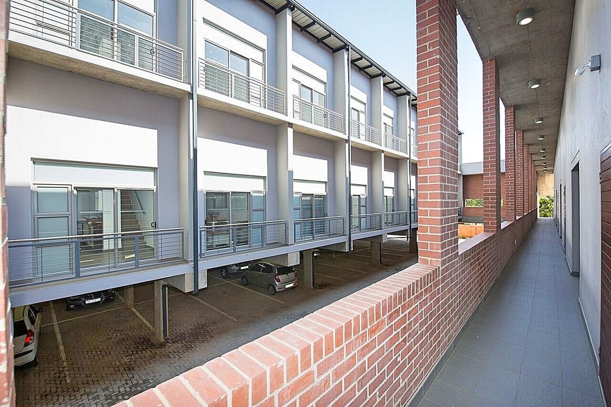 An exterior view of the apartment complex featuring a covered brick-pillared walkway overlooking the ground-level parking area and residential units.