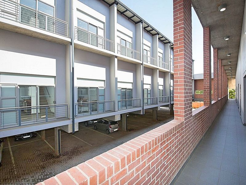 An exterior view of the apartment complex featuring a covered brick-pillared walkway overlooking the ground-level parking area and residential units.