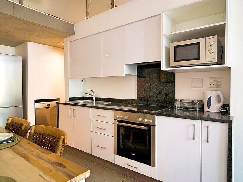 Modern kitchen featuring white cabinetry, granite countertops, integrated stainless steel oven, electric hob, and built-in microwave, offering a clean and functional workspace.