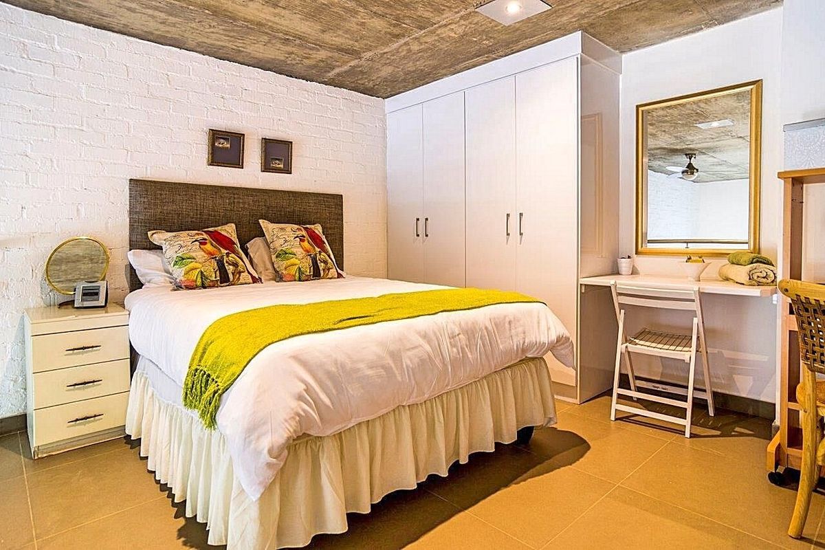 A modern bedroom featuring an exposed concrete ceiling, painted brick feature wall, built-in wardrobe, and a convenient integrated desk area.