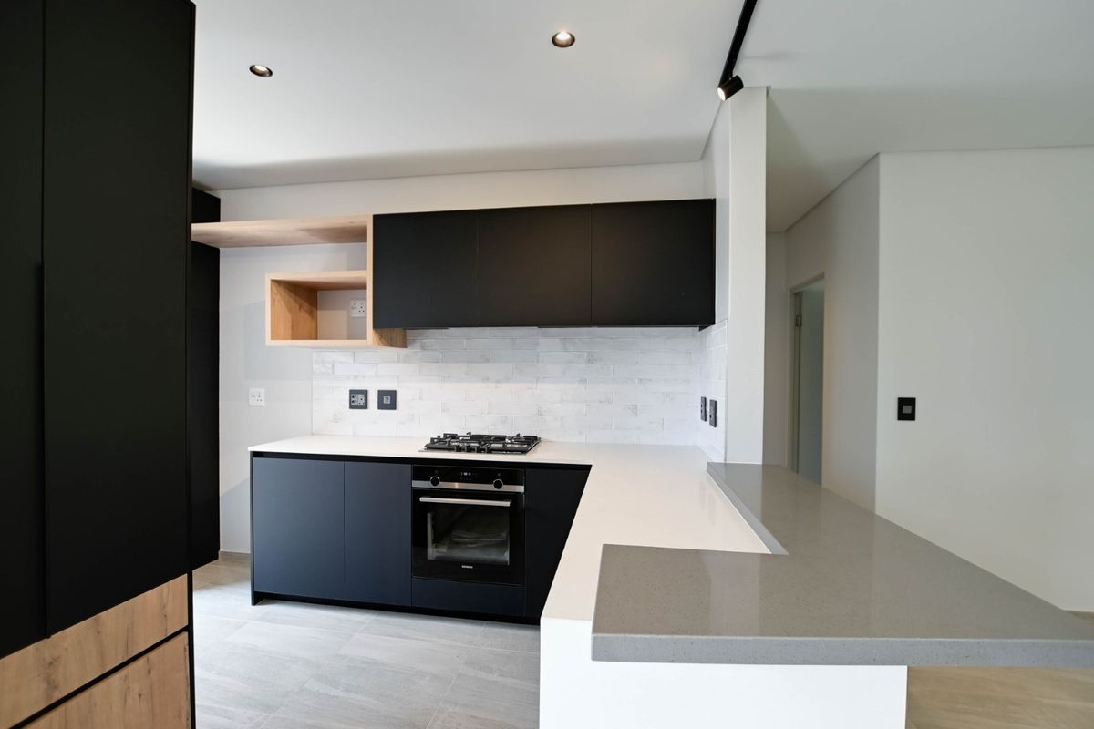 Modern kitchen featuring sleek black cabinetry, light wood accents, stone countertops, a gas hob, and a subway tile backsplash in a clean, contemporary design.
