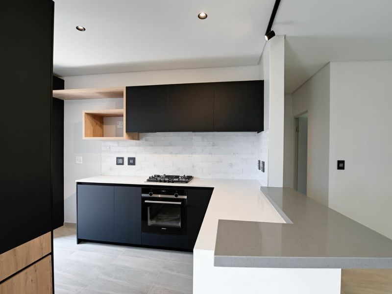 Modern kitchen featuring sleek black cabinetry, light wood accents, stone countertops, a gas hob, and a subway tile backsplash in a clean, contemporary design.