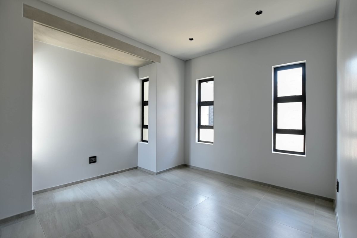 A bright, modern, and empty bedroom featuring neutral tiled flooring, clean white walls, and contemporary aluminium-framed windows.