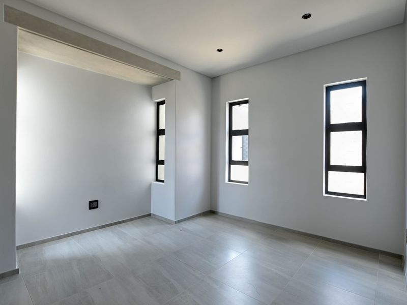 A bright, modern, and empty bedroom featuring neutral tiled flooring, clean white walls, and contemporary aluminium-framed windows.