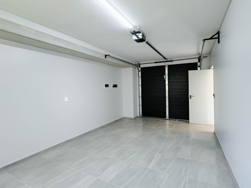 A clean, well-maintained garage featuring tiled flooring, an automated door, and direct side access.