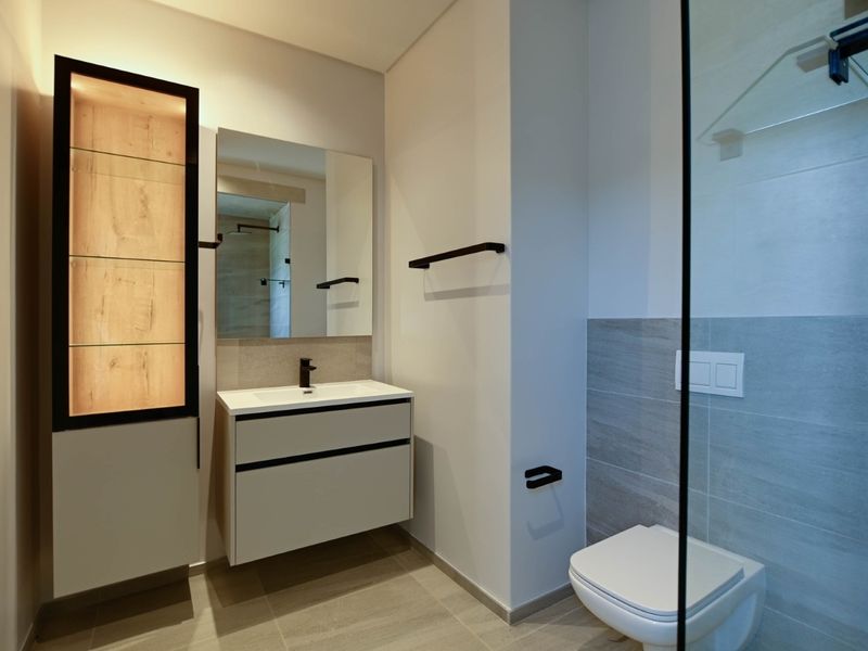 Modern bathroom featuring a wall-hung vanity, wall-hung toilet, glass shower enclosure, and contemporary tiled finishes with integrated lighting.
