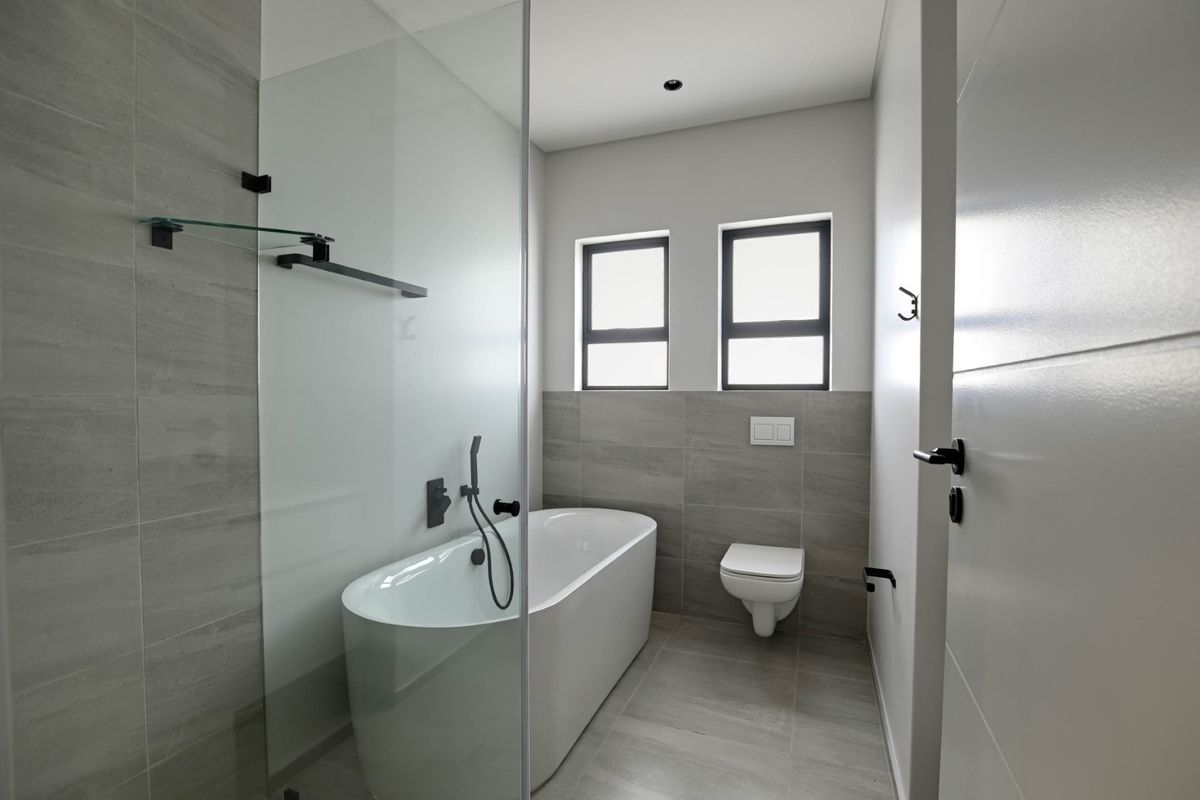 Modern bathroom featuring a sleek freestanding bathtub, glass shower screen, wall-mounted toilet, and contemporary grey tiling with matte black fixtures.