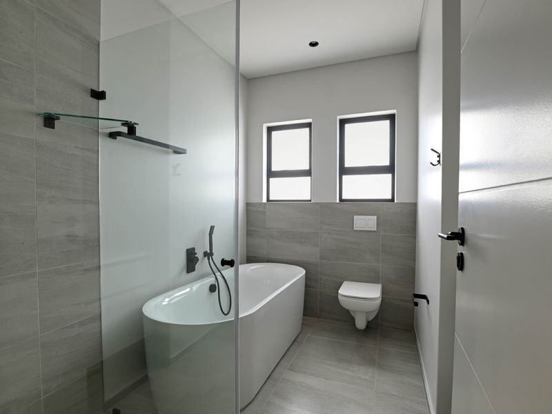 Modern bathroom featuring a sleek freestanding bathtub, glass shower screen, wall-mounted toilet, and contemporary grey tiling with matte black fixtures.