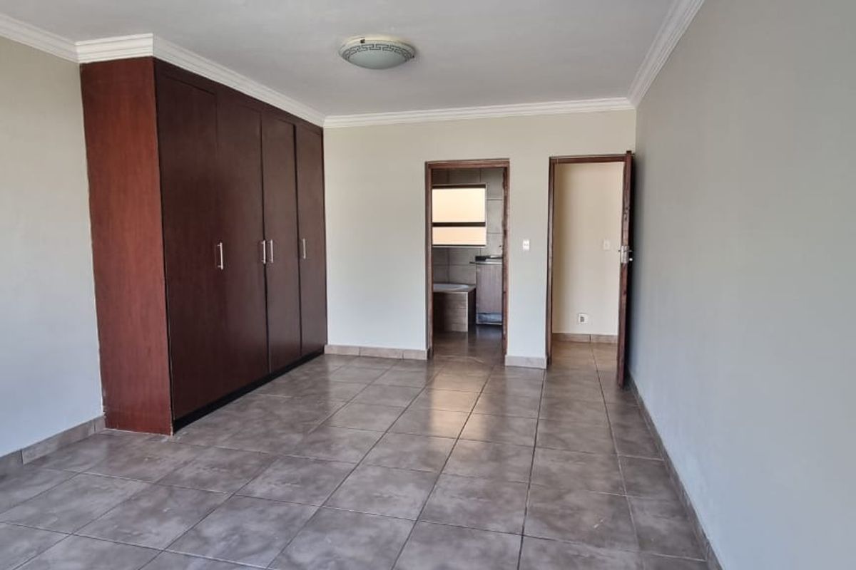 Spacious bedroom featuring neutral tiled flooring, built-in wooden cupboards, and direct access to an adjoining room.