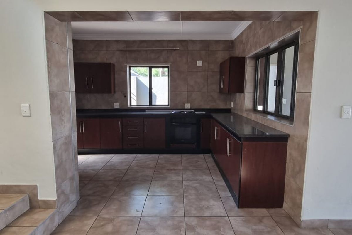 A functional kitchen featuring dark wood cabinetry, granite countertops, built-in oven, and tiled finishes throughout, offering a clean and practical workspace.