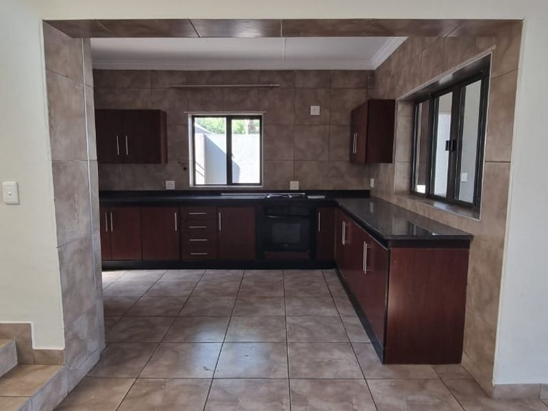 A functional kitchen featuring dark wood cabinetry, granite countertops, built-in oven, and tiled finishes throughout, offering a clean and practical workspace.