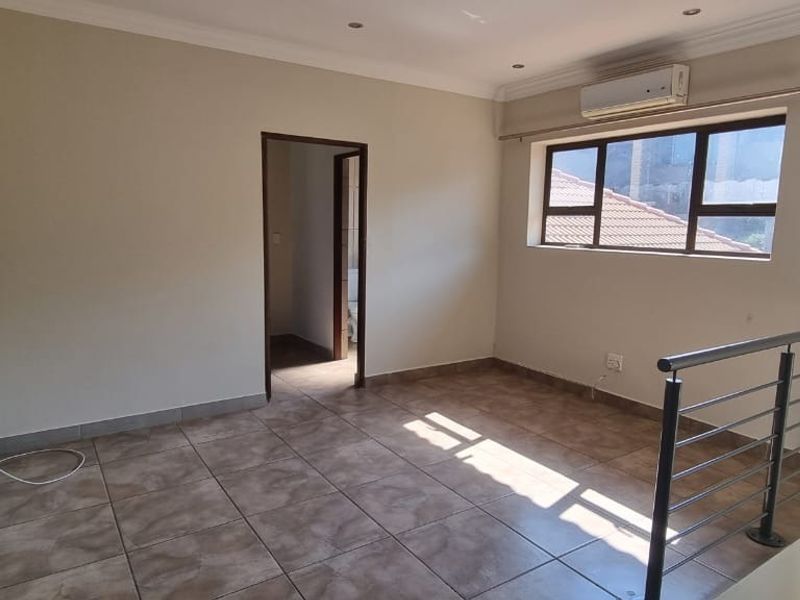 An empty, well-maintained living area featuring tiled flooring, a split-system air conditioner, and a modern metal balustrade overlooking the lower level.