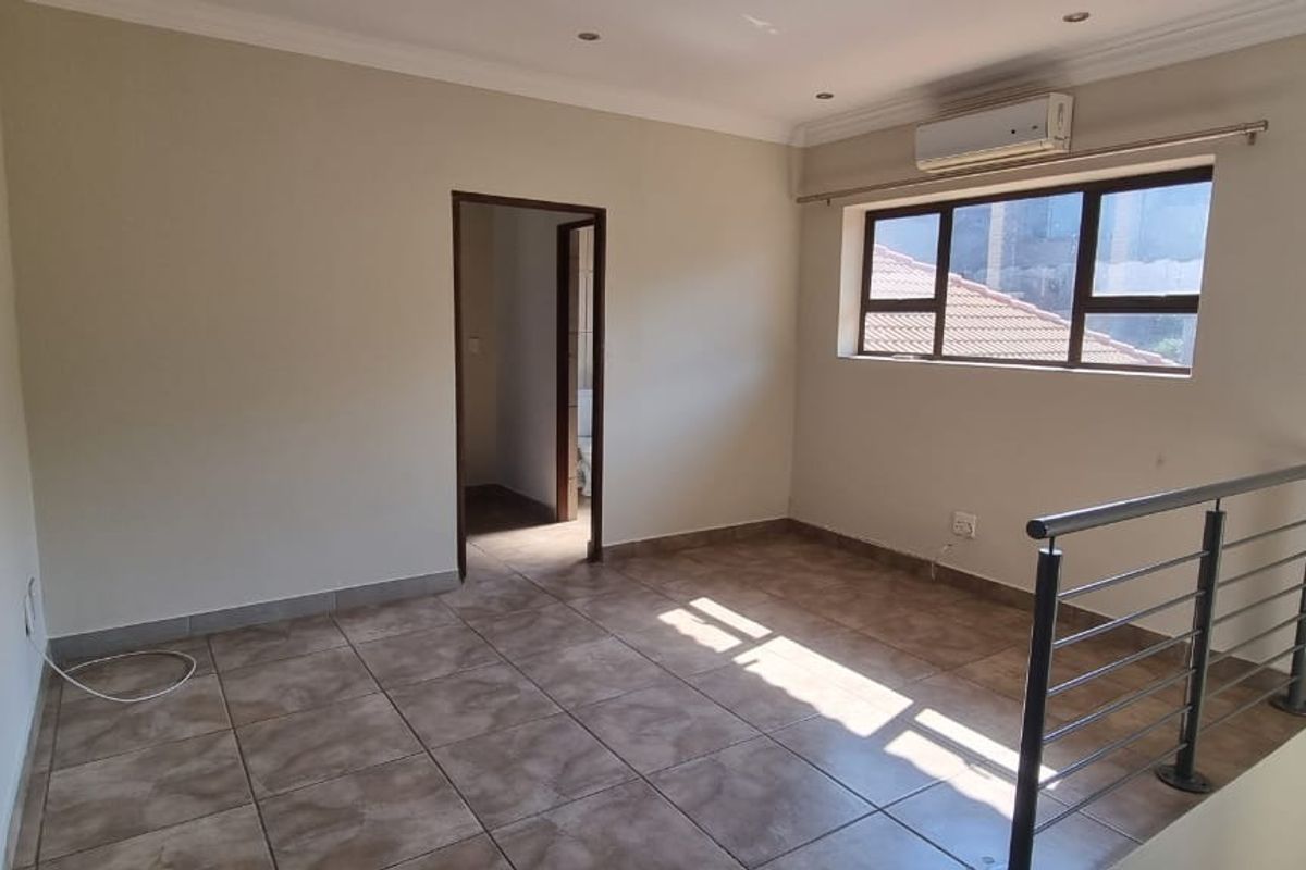An empty, well-maintained living area featuring tiled flooring, a split-system air conditioner, and a modern metal balustrade overlooking the lower level.
