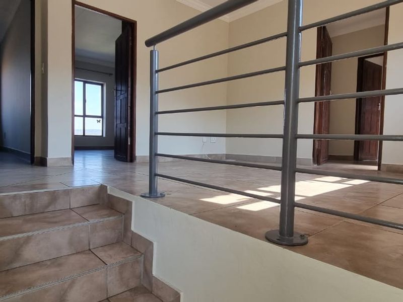 A spacious, empty hallway featuring tiled flooring and a modern metal balustrade, providing access to multiple rooms.