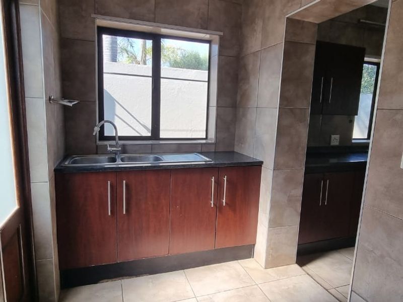 A functional scullery area featuring dark wood cabinetry, granite countertops, a double bowl sink, and neutral wall tiling.