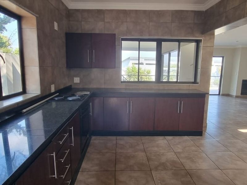 An open-plan kitchen featuring dark wood cabinetry, granite countertops, and tiled flooring, flowing into a spacious living area with a fireplace.
