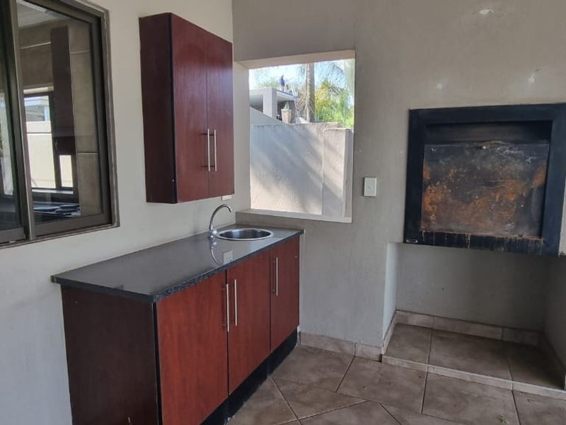 Covered patio area featuring a built-in braai, granite-topped kitchenette with sink, and tiled flooring, suitable for outdoor entertaining.