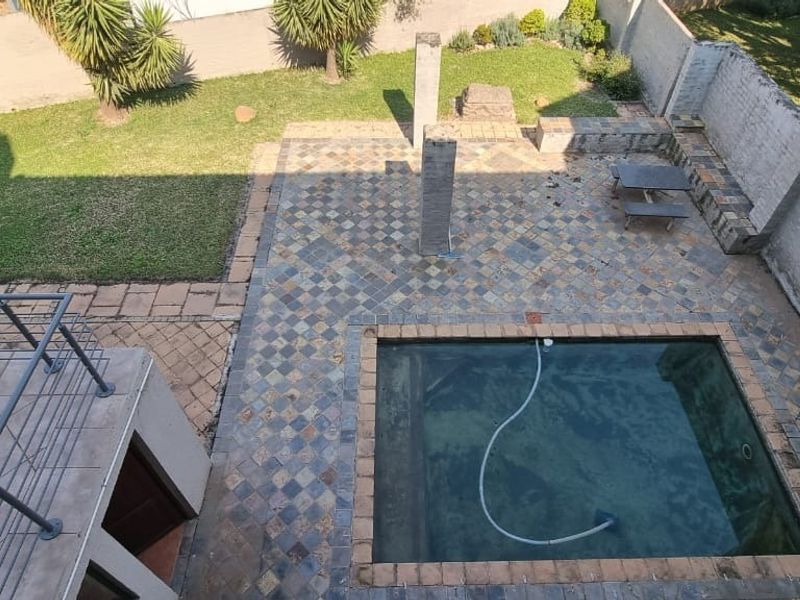 An elevated view of a backyard featuring a swimming pool, paved patio area, and surrounding lawn with boundary walls.