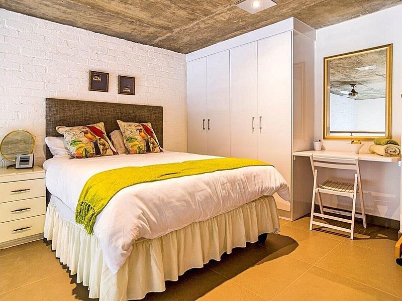 A well-maintained bedroom featuring an exposed concrete ceiling, painted brick feature wall, tiled flooring, and ample built-in wardrobe storage.