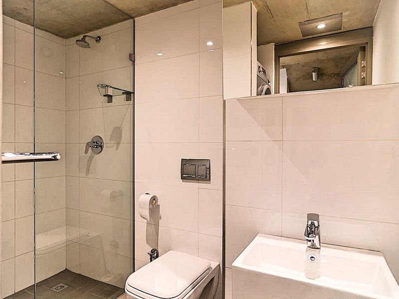 Modern bathroom featuring a glass-enclosed shower, wall-mounted toilet, vanity basin with chrome fixtures, and clean tiled finishes.