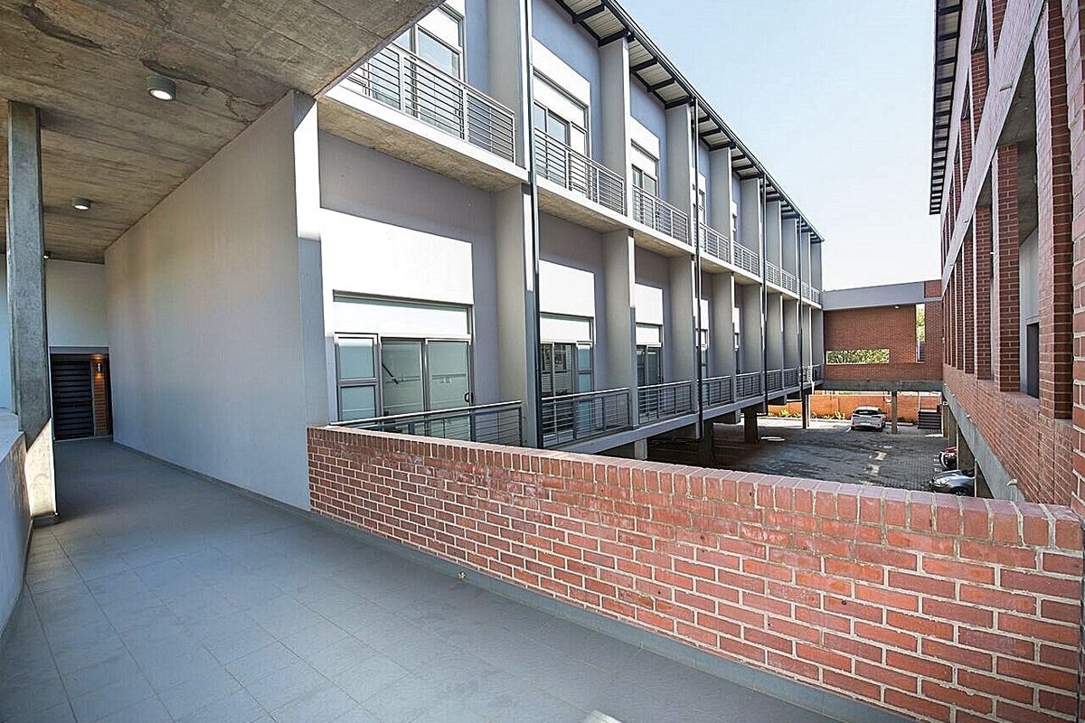 Exterior view of an apartment complex featuring a covered walkway, brick architectural details, and access to a paved parking area.