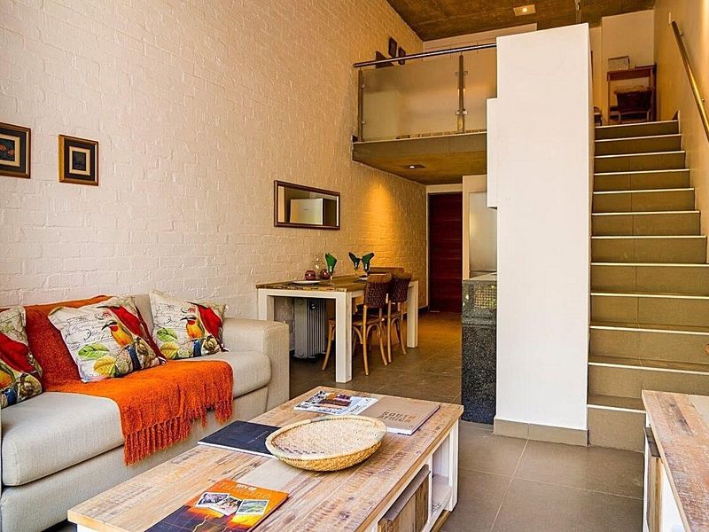 Open-plan living area featuring high ceilings, exposed concrete, a mezzanine level with glass balustrade, and a staircase leading to the upper floor.