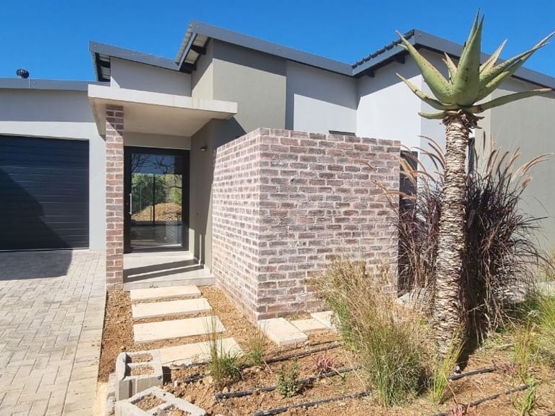 Modern retirement village residence featuring a brick facade, paved driveway, single garage, and a landscaped front garden with an integrated irrigation system.