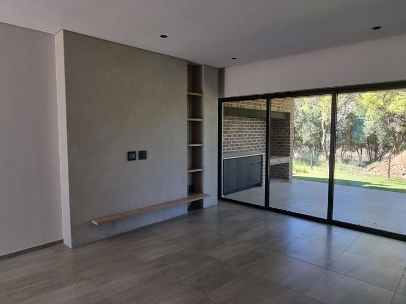 Modern, light-filled living room featuring large sliding glass doors, tiled flooring, and a contemporary feature wall with built-in shelving.