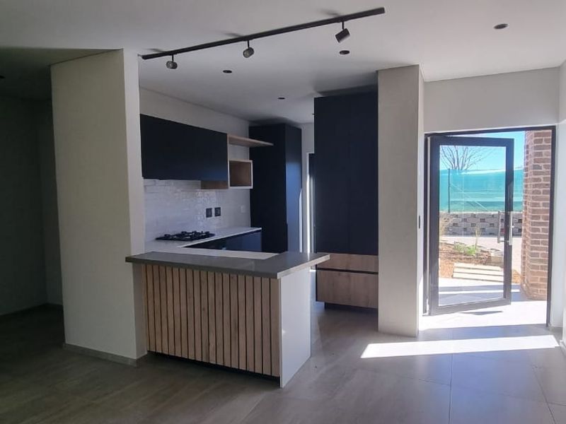 Modern open-plan kitchen featuring sleek dark cabinetry, stone countertops, a breakfast bar, and direct access to an outdoor area.