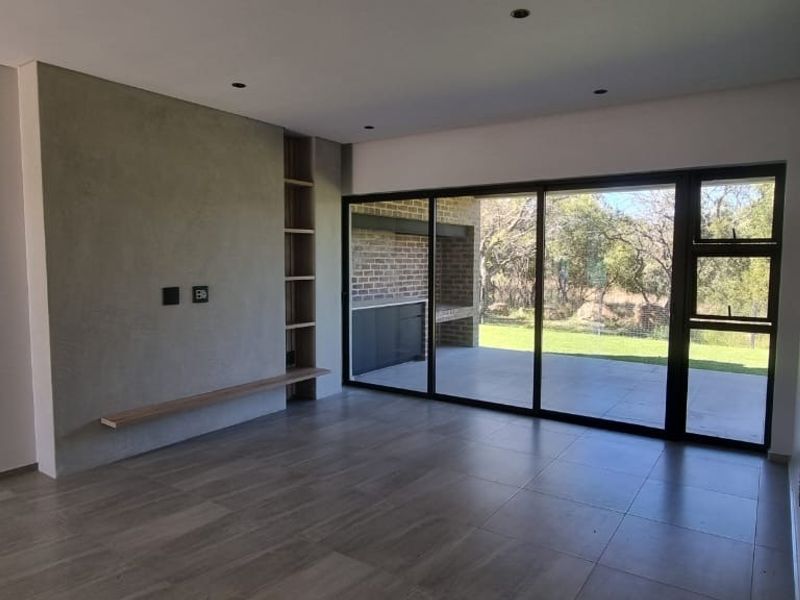 Modern, open-plan living area featuring large sliding glass doors, tiled floors, recessed lighting, and a contemporary feature wall with built-in shelving.