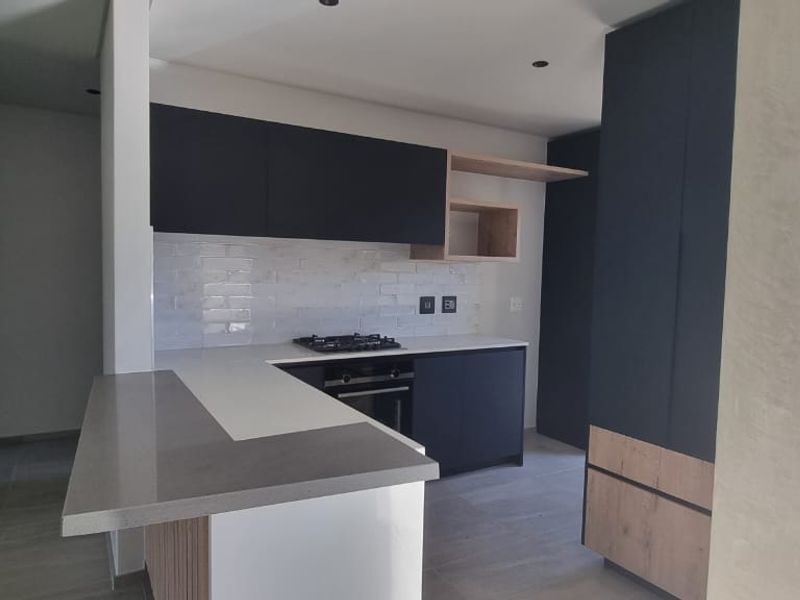 Modern kitchen featuring dark cabinetry, light wood accents, quartz countertops, a gas hob, and a subway tile backsplash in an open-plan layout.