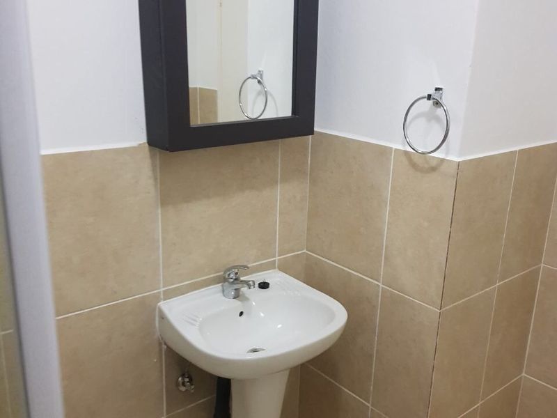 A functional bathroom featuring a pedestal basin with a chrome mixer tap, wall-mounted medicine cabinet, and neutral ceramic wall tiling.