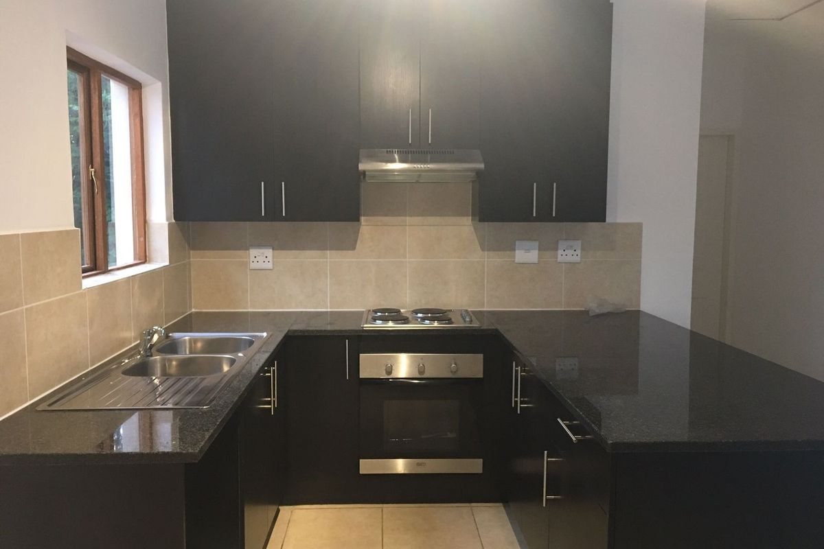 A modern, well-maintained kitchen featuring dark cabinetry, granite countertops, stainless steel appliances, and a tiled backsplash.