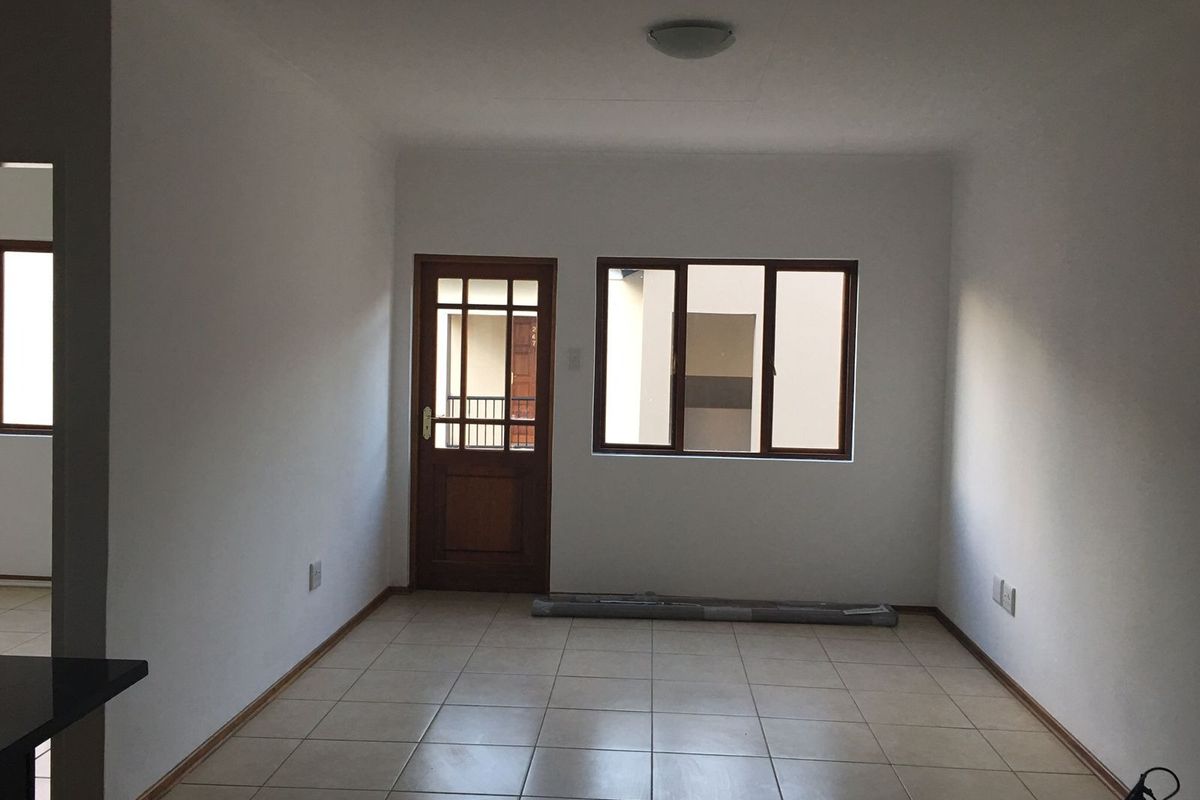 An empty, neutrally painted living area featuring tiled flooring, a timber-framed entrance door, and a matching window, providing a clean canvas for personalization.