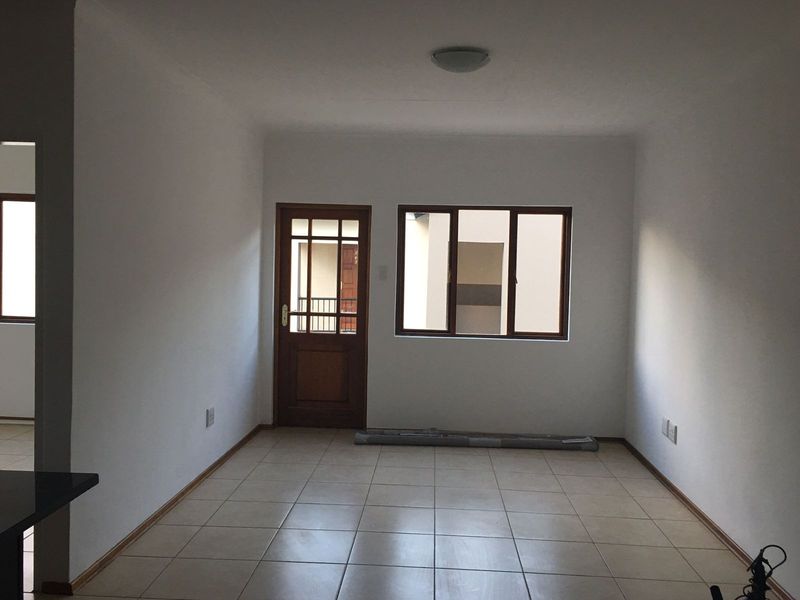 An empty, neutrally painted living area featuring tiled flooring, a timber-framed entrance door, and a matching window, providing a clean canvas for personalization.