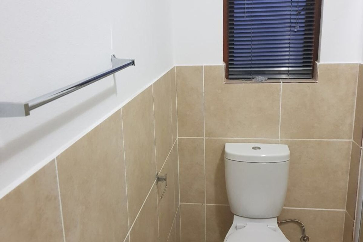 A functional bathroom featuring neutral ceramic wall tiles, a standard toilet, and a chrome towel rail.