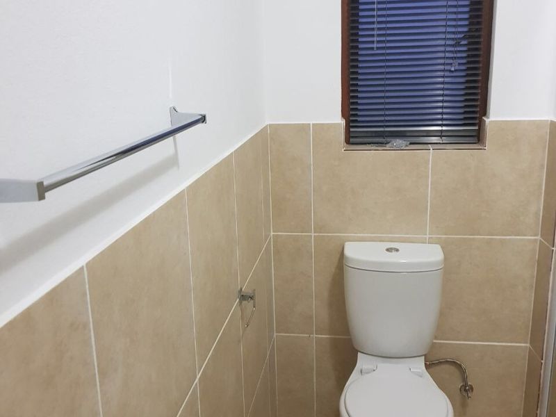 A functional bathroom featuring neutral ceramic wall tiles, a standard toilet, and a chrome towel rail.