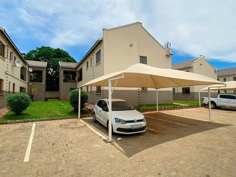 Exterior view of the apartment complex featuring a paved parking area with shade cloth carports and well-maintained communal garden spaces.
