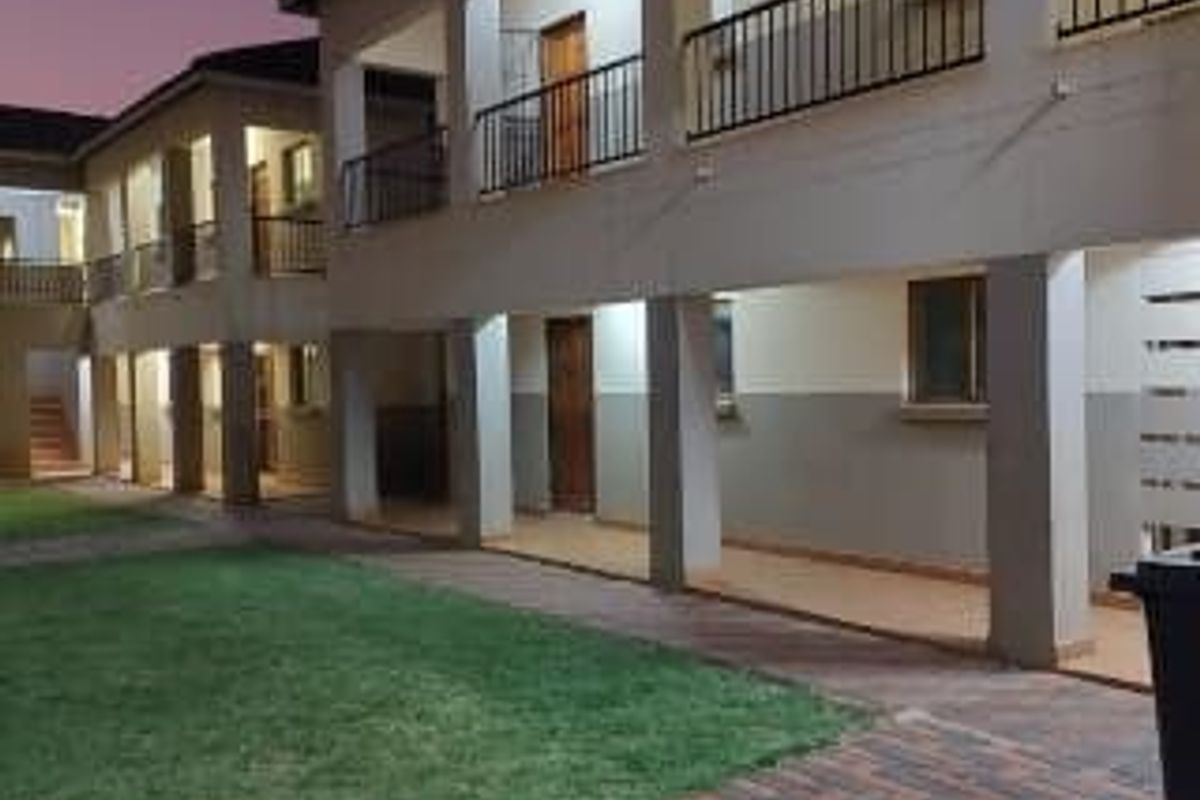 A view of the apartment complex exterior featuring covered walkways, balconies with railings, and a well-maintained lawn area at dusk.