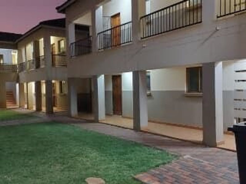 A view of the apartment complex exterior featuring covered walkways, balconies with railings, and a well-maintained lawn area at dusk.
