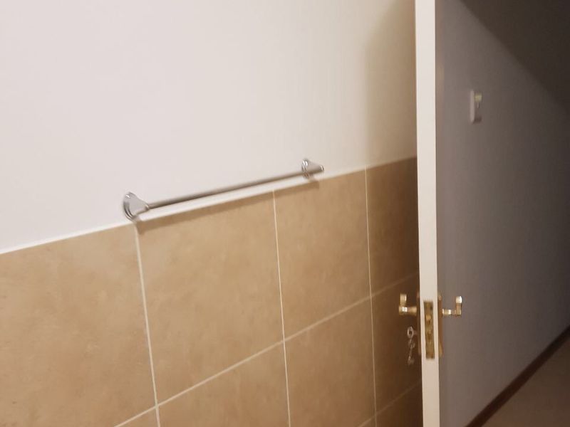A view of a bathroom wall featuring neutral ceramic tiling and a chrome towel rail, showing a simple and functional space.