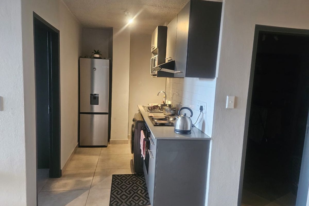 Compact kitchen featuring modern grey cabinetry, tiled flooring, a subway tile backsplash, and integrated hob with extractor fan.