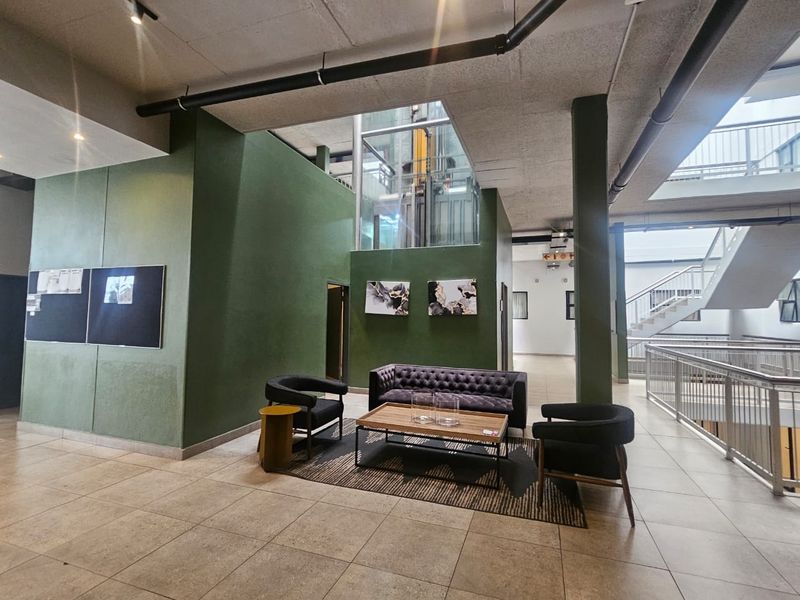 Modern apartment building lobby featuring a glass elevator, industrial-style exposed ceiling pipes, and tiled flooring with an open-plan layout.
