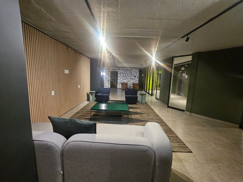Modern living area featuring contemporary timber slat wall paneling, exposed concrete ceilings, and sleek track lighting in a well-maintained apartment building.