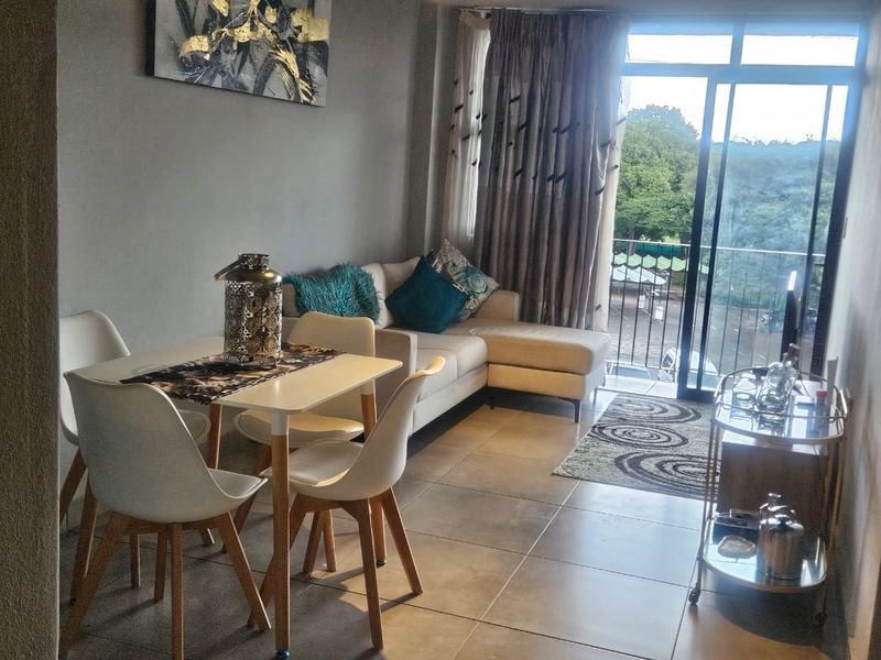 An open-plan living and dining area featuring tiled flooring and a large sliding glass door leading to a balcony with outdoor views.