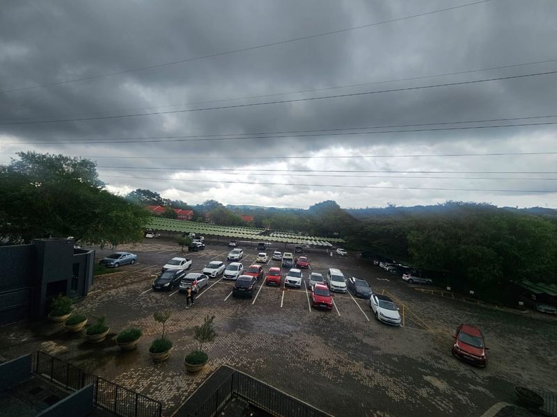Elevated view overlooking a paved parking lot with covered bays and surrounding greenery under an overcast sky.