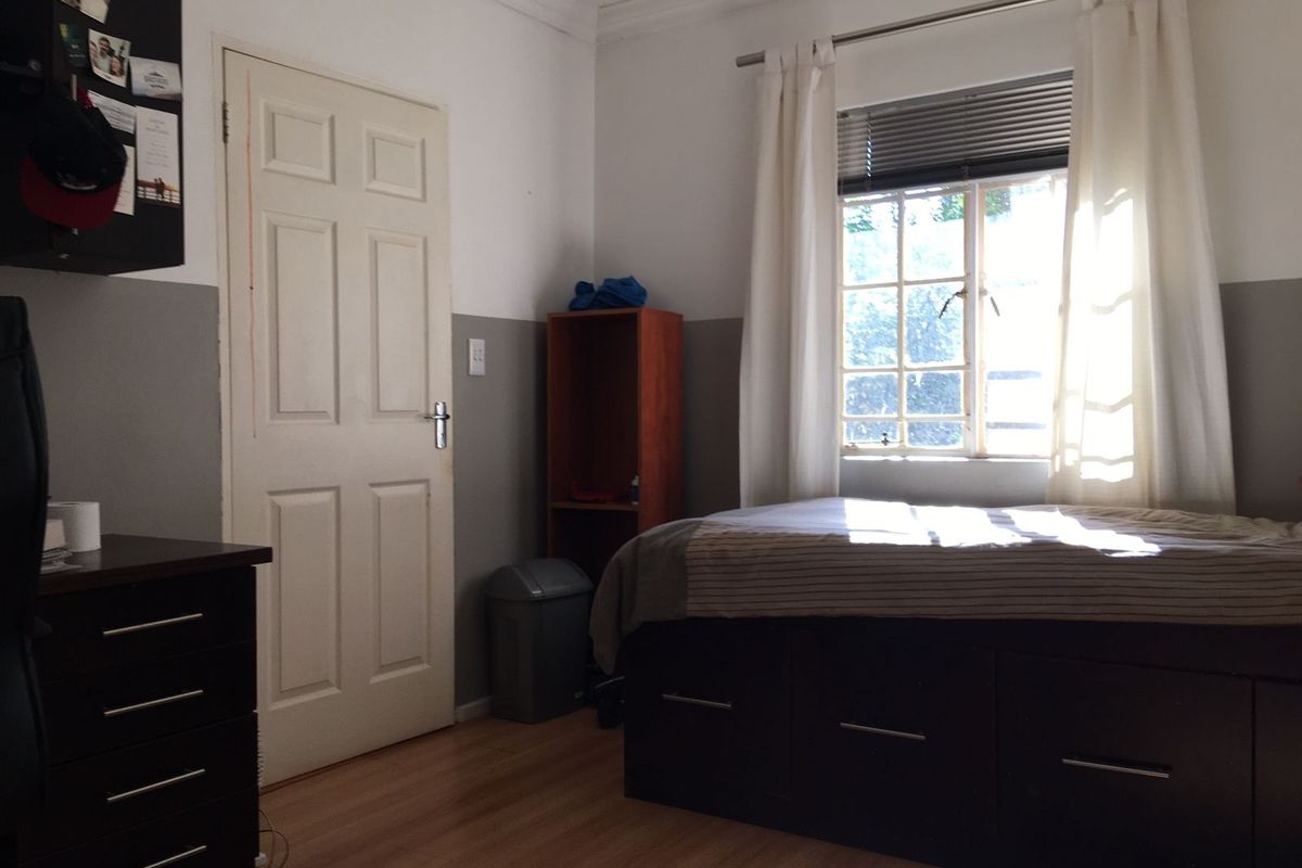 A bedroom featuring laminate flooring, a window with blinds, and a classic panel door.